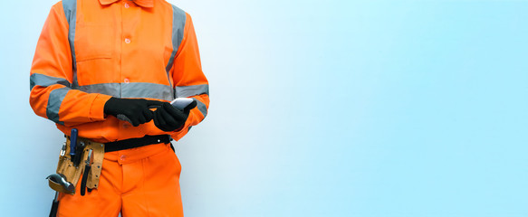 Builder worker is holding in hand a mobile phone isolated on a blue background with copy space....