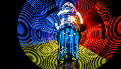 Tricolor neon lights of spinning carousel with dark sky in amusement park, long exposure effect
