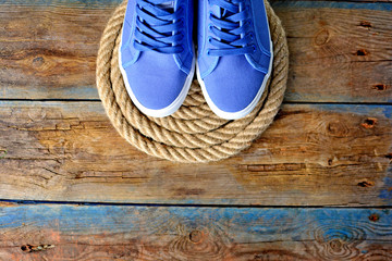 Blue sneakers shoes on a rope spiral, on a wooden weathered terrace. Yacht style concept. Template for avdertisement banner.