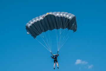 Skydiver with grey parachute in blue sky