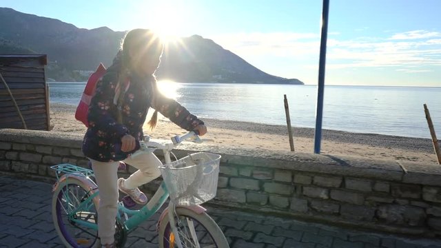six year old girl rides a bicycle to school in the morning along the seafront
