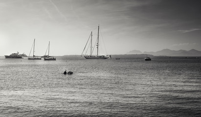 Black and white picture of the yachts and sailboats at anchor in Golfe Juan at the French beach resort of Juan-les-Pins with the island Ile Sainte-Marguerite in the background