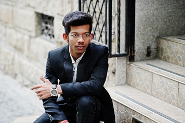 Obraz premium Young indian man on suit and glasses posed outdoor and sitting on stairs.