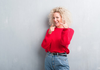 Young blonde woman with curly hair over grunge grey background pointing fingers to camera with happy and funny face. Good energy and vibes.