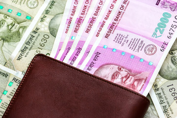 Close up view of leather wallet with brand new indian 2000 rupees banknotes. 500 rupee banknotes in background.