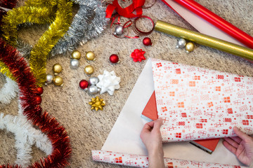Female hands wrapping a book for Christmas present, top view