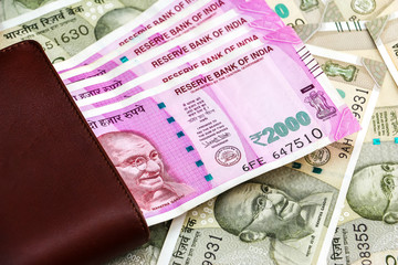 Close up view of leather wallet with brand new indian 2000 rupees banknotes. 500 rupee banknotes in background.