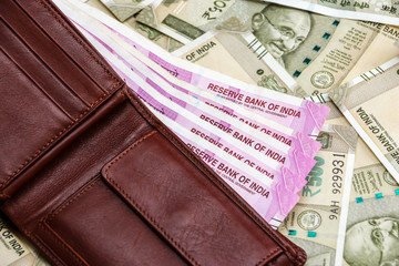 Close up view of leather wallet with brand new indian 2000 rupees banknotes. 500 rupee banknotes in background.