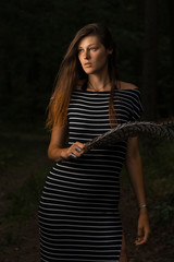 Fantasy portrait of the young woman with bird feathers in the dark woods.