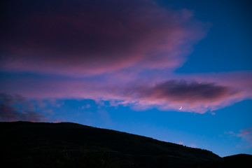 Moon with clouds at sunset in a growing phase, before hiding behind the mountain