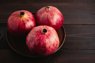 Group of red pomegranate fruits in the brown plate on a dark wooden background