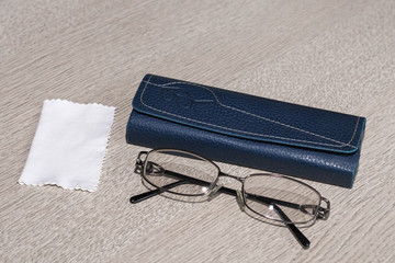 Tinted glasses and case with glasses cleaning cloth on grey wood table