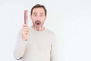 Senior man holding hair comb over isolated background scared in shock with a surprise face, afraid and excited with fear expression