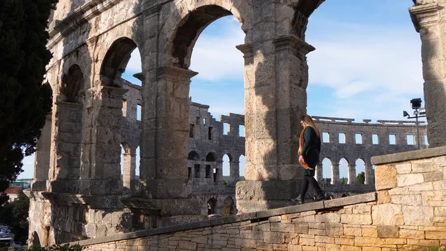 Slow motion footage of female walking on wall in front of Pula Arena in Croatia.