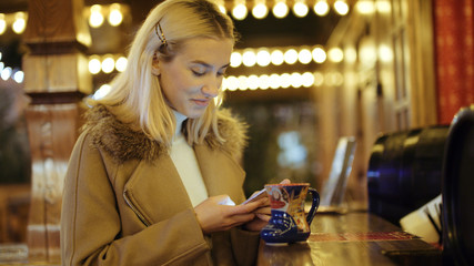 Woman using smartphone on christmas market. Girl enjoying winter holiday season. Concept of  social networking, communicating, using app. Blurred Christmas lights on background.
