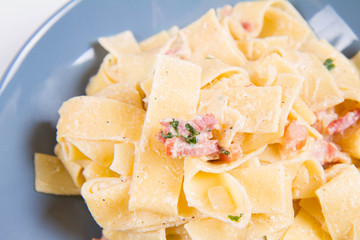 Pappardelle Carbonara on a blue plate on a white background