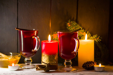 Mulled wine and burning candle on dark background. Christmas mulled wine, cinnamon sticks and honey. Alcohol drink of wine and honey. Festive drink and Christmas tree branches
