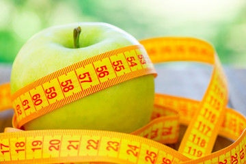 Green apple with measuring tape on wooden background. Apples and sewing tape measure on a wooden table. To lose weight and eat a low calorie apple to lose weight