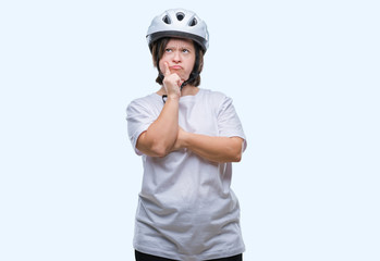 Young adult cyclist woman with down syndrome wearing safety helmet over isolated background with hand on chin thinking about question, pensive expression. Smiling with thoughtful face. Doubt concept.