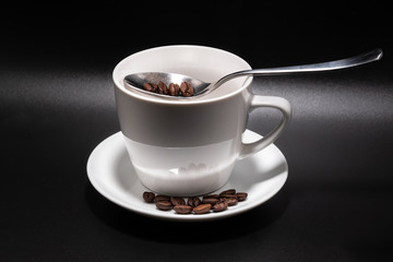 White cup, saucer and spoon on a black background