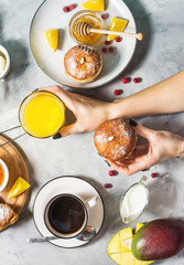 Female hands hold donut and glass. Breakfast served with coffee, orange juice, croissants and fruits on concrete background