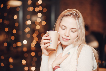 Woman holding paper cup of coffee in hands, background cafe bokeh