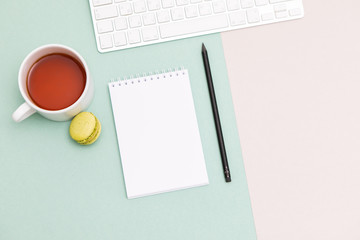 Office desk mock up template with clean notebook and Cup of tea and macaron on Pastel Background. Top view, flat lay.
