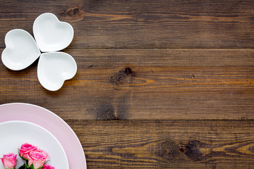 Fototapeta premium Simple color table setting for celebration with roses, pink plates and heart-shaped saucers on wooden table background top view mock up