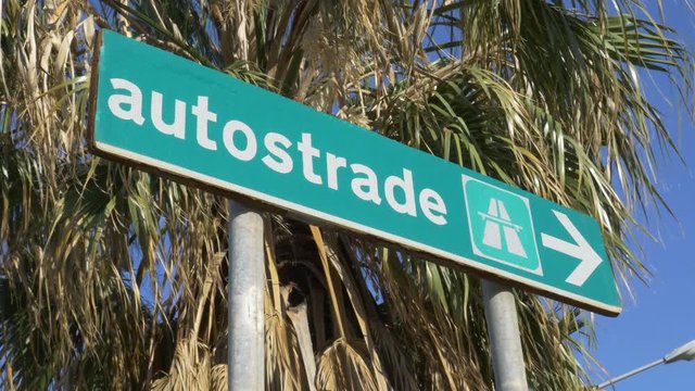 Autostrade sign for highway. Palm trees blowing in the wind. Palermo, Sicily, Italy.