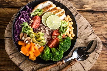 Photo sur Plexiglas Plats de repas Buddha bowl salad with chicken fillet, brown rice, avocado, pepper, tomato, broccoli, red cabbage, chickpea, fresh lettuce salad, pine nuts and walnuts. healthy food. balanced diet eating. Top view