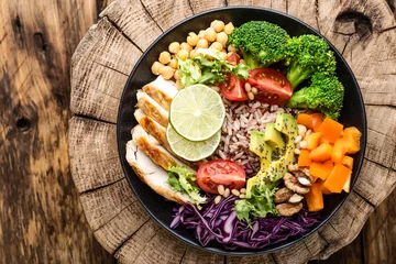Fotobehang Gerechten Buddha bowl salad with chicken fillet, brown rice, avocado, pepper, tomato, broccoli, red cabbage, chickpea, fresh lettuce salad, pine nuts and walnuts. healthy food. balanced diet eating. Top view