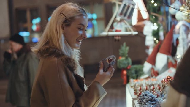 Young blonde girl having fun at christmas market in a city. Happy attractive woman in a christmas market at night. Beautiful bokeh lights background.