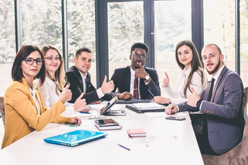 Group of business people with businessman leader in the center at the table showing a thumbs up, which means a good deal