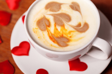 Valentine's day background. A white Cup of cappuccino coffee with a latte art in the form of hearts. Coffee on a wooden table covered with red hearts. Meeting with your loved one over a Cup of coffee