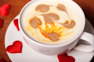 Valentine's day background. A white Cup of cappuccino coffee with a latte art in the form of hearts. Coffee on a wooden table covered with red hearts. Meeting with your loved one over a Cup of coffee