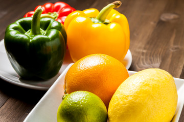 Citrus fruit and bell peppers in a white square bowls on a wooden table