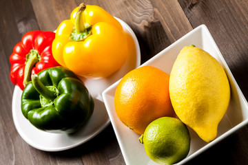Citrus fruit and bell peppers in a white square bowls on a wooden table