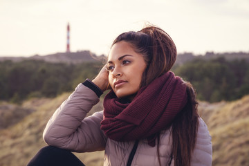 Portrait of exotic woman with winter clothes on in front of a lighthouse.