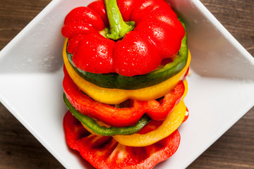 Fresh vibrant bell pepper slices in a white square bowl isolated on wooden surface