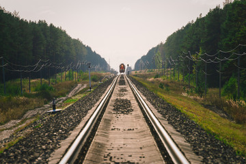 Mystic train travels by rail along forest. Railway traffic light and locomotive on railroad in distance. Mirage on railway track. Atmospheric landscape.