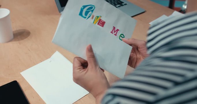 Over the shoulder shot of female office worker opens a ransom letter from blackmailer saying Give me donuts and nobody gets hurt. 4K UHD