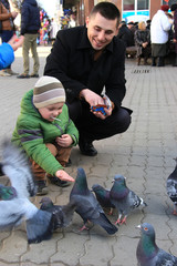 The boys with mother on the square feed pigeons