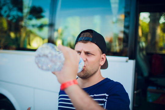 Handsome Man Drinking Water After Running Outdoors On The Background Of The Bus, Tourist.