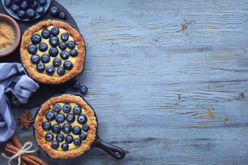 Delicious Blueberry tartlets with vanilla custard cream on on blue wooden background