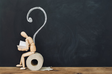 Wooden figure sit on a roll of toilet paper against the background of a drawn question mark on a...