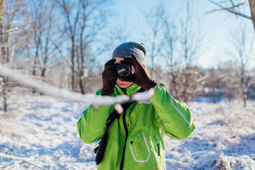 Fototapeta na wymiar Young photographer takes pictures of winter forest using camera. Young man shooting photos outdoors