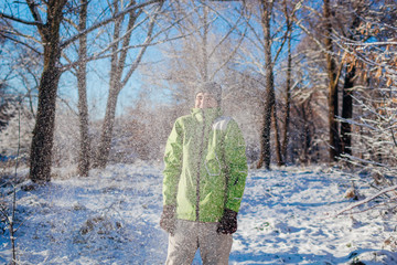 Young man throwing snow in winter forest. Guy having fun outdoors. Man feeling cold under falling...