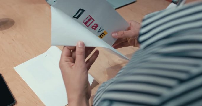 Over the shoulder shot of female office worker opens a ransom letter from blackmailer saying I have your coffee. 4K UHD