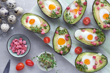Keto diet dish: Avocado boats with quail eggs, ham cubes and cress sprouts on light stone serving...