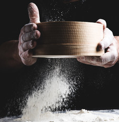 round wooden sieve with flour in male hands, the chef sifts white wheat flour